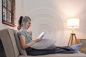 Happy young woman read book on sofa at home. Lifestyle freelance relax in living room. Lifestyle Concept