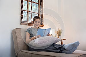 Happy young woman read book on sofa at home. Lifestyle freelance relax in living room. Lifestyle Concept