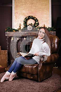 Happy young woman reading book in front of christmas tree