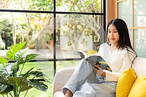 Happy young woman reading book on sofa at home.  Lifestyle freelance relax and chill drinking coffee in living room,