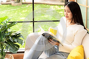 Happy young woman reading book on sofa at home. Lifestyle freelance relax and chill drinking coffee in living room