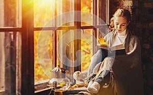 Happy young woman reading book by window in fall