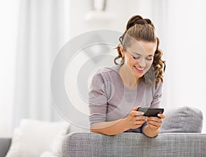 Happy young woman reading sms while sitting on couch