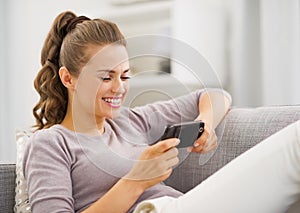 Happy young woman reading sms while sitting on couch