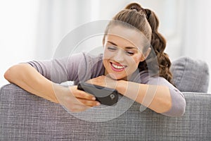 Happy young woman reading sms while sitting on couch