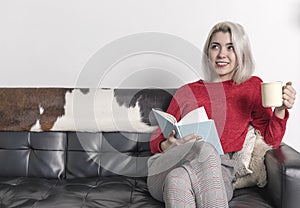 Happy young woman reading storybook on couch at home