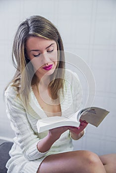 Happy young woman reading storybook on couch at home, winter, coziness, leisure and people concept - close up of young woman