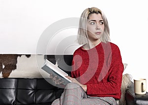 Happy young woman reading storybook on sofa at home while looking aside