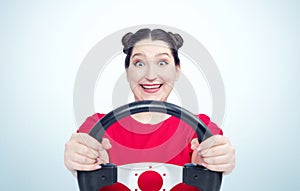 Happy young woman in red t-shirt with steering wheel on light blue background, car driver concept