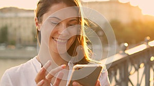 Happy young woman relaxing outdoors. Beautiful girl chatting on her smartphone. Summer sun shining