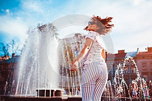 Happy young woman running and dancing by fountain on summer street