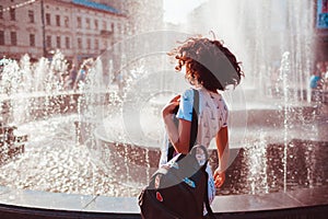 Happy young woman running and dancing by fountain on summer street