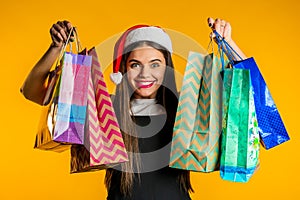 Happy young woman in Santa hat with colorful paper bags after shopping isolated