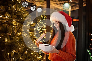 Happy young woman in santa hat opens a surprise gift on christmas night