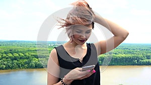 Happy young woman sending sms, texting in the park. Hair blowing in wind