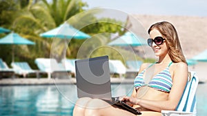Happy young woman in shades with laptop on beach