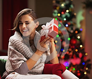 Happy young woman shaking present box near christmas tree