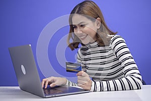 Happy young woman is shopping online via laptob , holding credit card