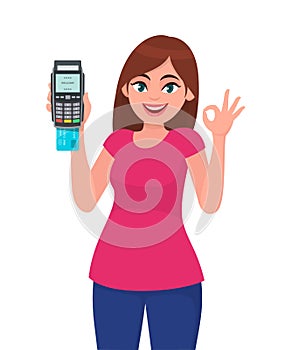 Happy young woman showing/holding pos payment terminal or credit/debit cards swiping machine, gesturing okay/OK sign.