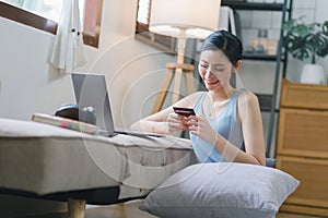 A happy young woman is shown shopping online using her laptop and credit card at home.