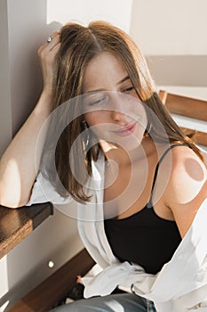Happy young woman sit relaxing in comfortable chair feel peaceful enjoy sun near big windows, smiling girl rest calm