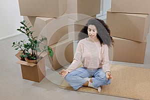 happy young woman sits in lotus position and meditates among packed boxes of personal belongings