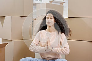 happy young woman sits in lotus position and meditates among packed boxes of personal belongings