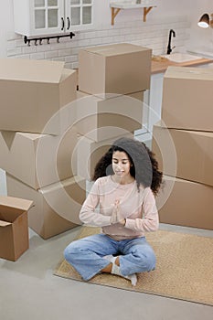 happy young woman sits in lotus position and meditates among packed boxes of personal belongings