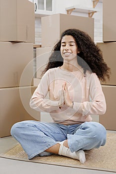 happy young woman sits in lotus position and meditates among packed boxes of personal belongings