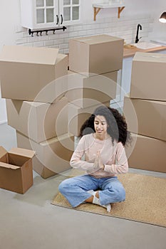 happy young woman sits in lotus position and meditates among packed boxes of personal belongings