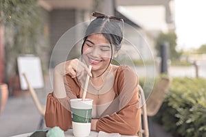 A happy young woman sits outside the coffee place and smiles after taking a sip of her cold fruit shake