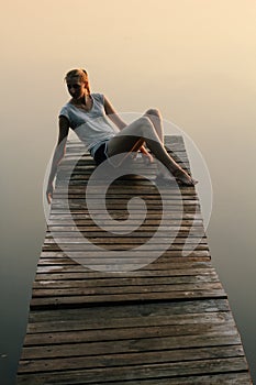 Happy young woman sits on a pier on a lake by the water