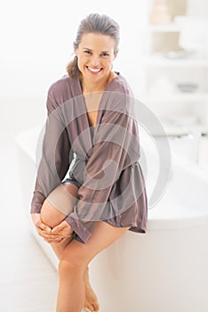 Happy young woman sitting on bathtub