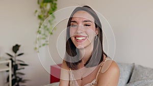 Happy young woman sitting on bed while looking at camera showing toothy smile