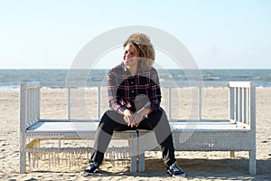 Happy young woman sitting on bench at the beach