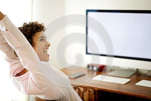Happy young woman sitting by computer with arms raised