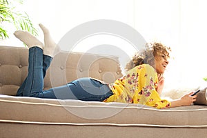 Happy young woman sitting on couch at home with mobile phone