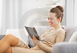 Happy young woman sitting on couch and working on tablet pc