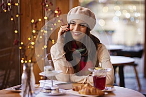 Happy young woman sitting at desk in the cafe and talking on her mobile phone