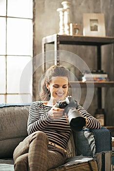 Happy young woman sitting on divan and using dslr