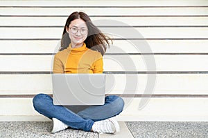 Happy young woman sitting on the floor with crossed legs and using laptop on gray background, Portrait of a happy young woman sitt