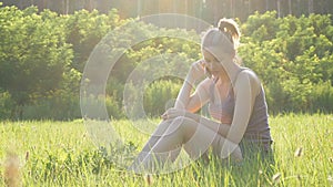 Happy young woman sitting on green lawn and talking on the phone or smartphone