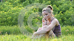 Happy young woman sitting on green lawn and talking on the phone or smartphone