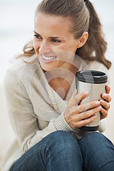 Happy young woman sitting on lonely beach with cup of beverage