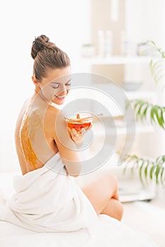 Happy young woman sitting on massage table with honey plate