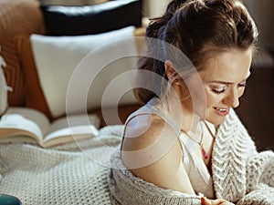 Happy young woman sitting near divan in modern living room