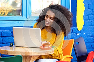 Happy young woman sitting at outdoor cafe using laptop