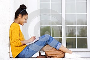 Happy young woman sitting outdoors writing a book