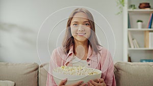 A Happy Young Woman Sitting on the Sofa Eating Popcorn and Watching TV.