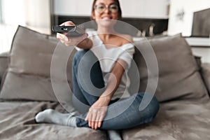 Happy young woman sitting on sofa at home watch TV.